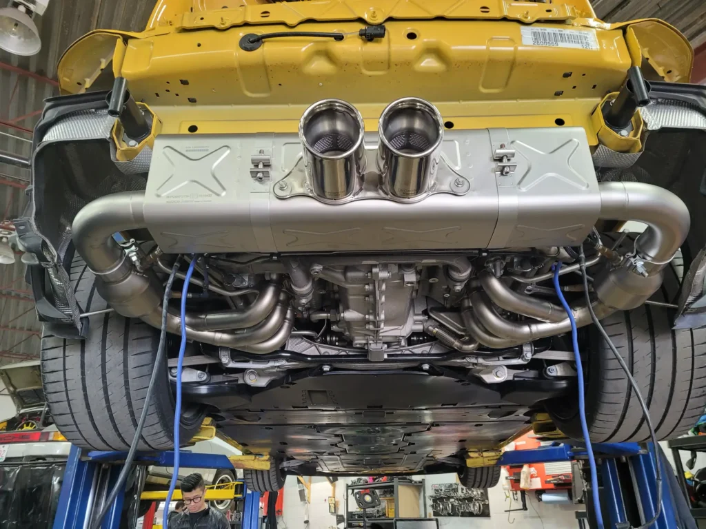 Underside of a yellow Porsche 911 on the lift showing the exhaust and engine