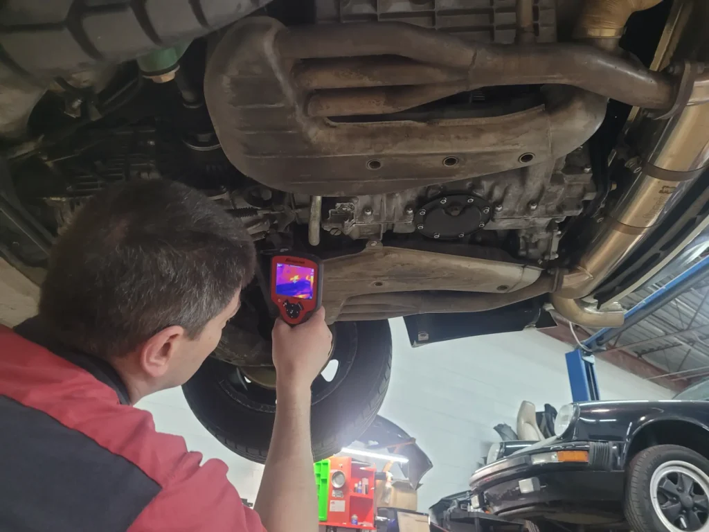Technician checking the underside of a car on a lift with a thermal camera at Alpine Autowerks