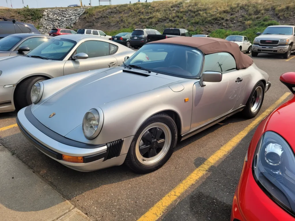 Silver Porsche 911 Speedster with a burgundy roof in a parking lot