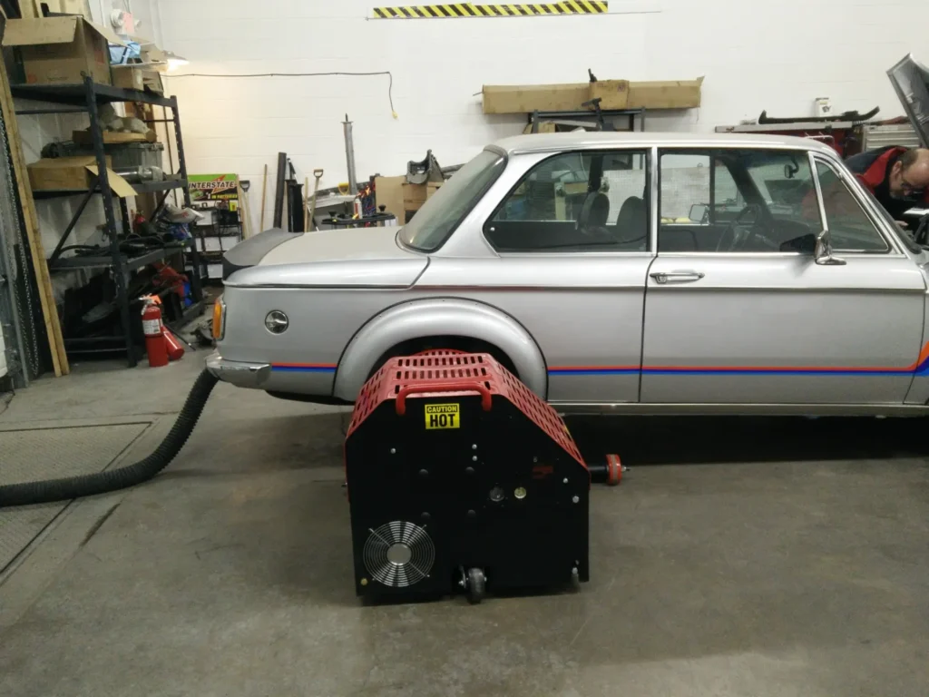 Silver BMW 2002 with a cooling fan and extraction hose set up in the shop