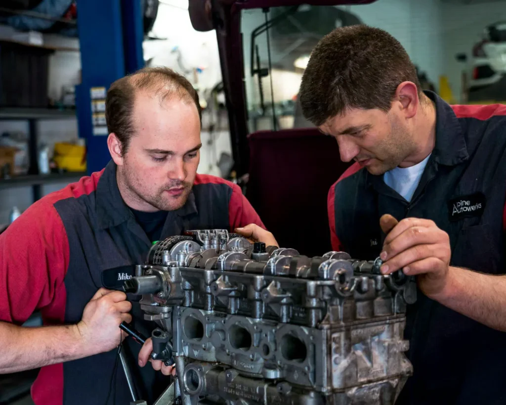 Two Alpine Autowerks technicians working on an engine on a stand
