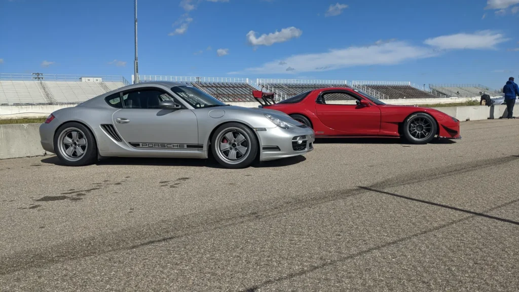 Silver Porsche Cayman and a red sports car in a track paddock
